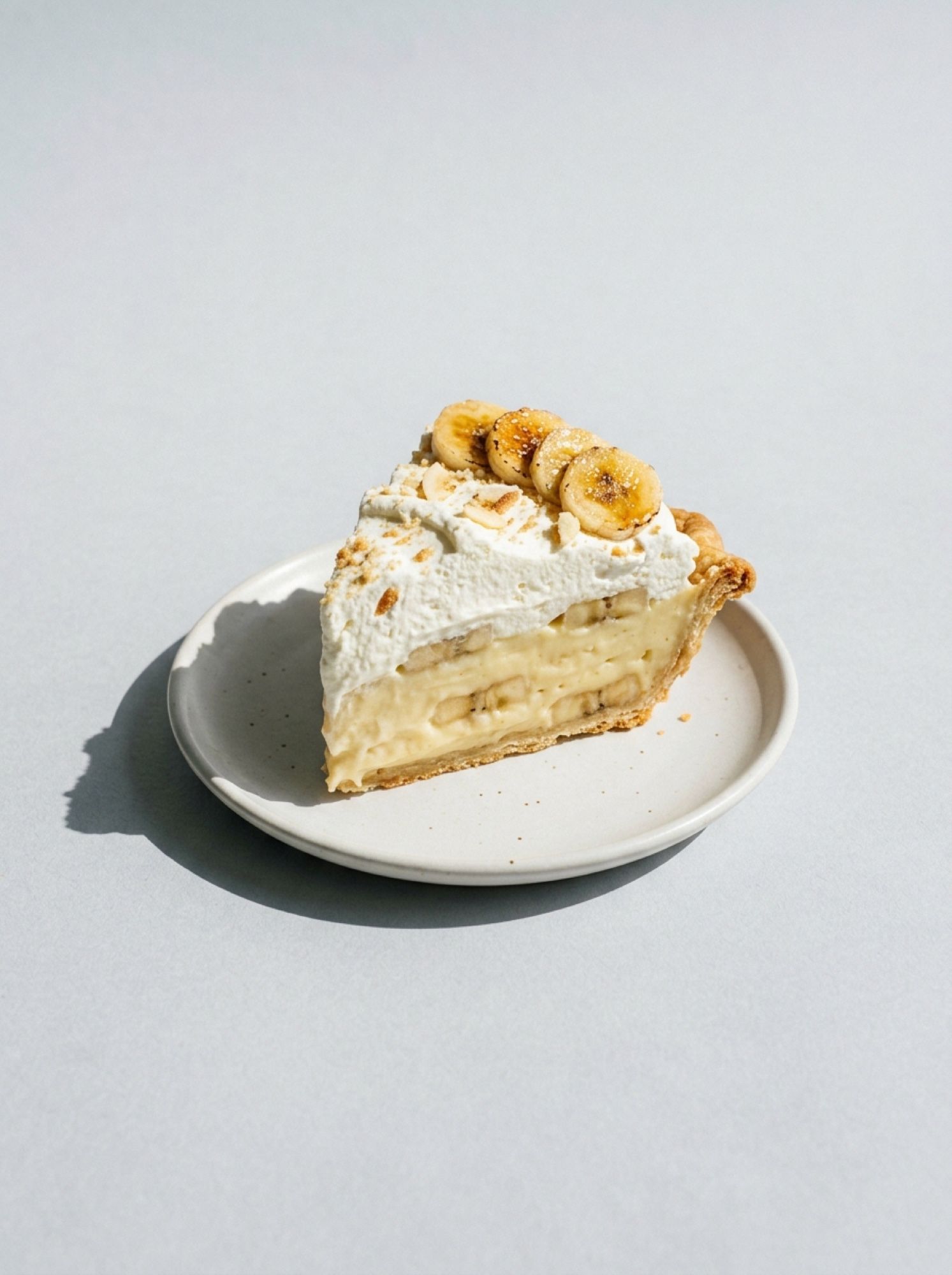 A slice of banana cream pie with sliced banana, custard and whipped cream on a white plate