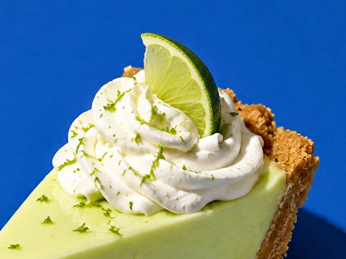 Close-up of a key lime pie slice topped with whipped cream, lime zest and a lime wedge